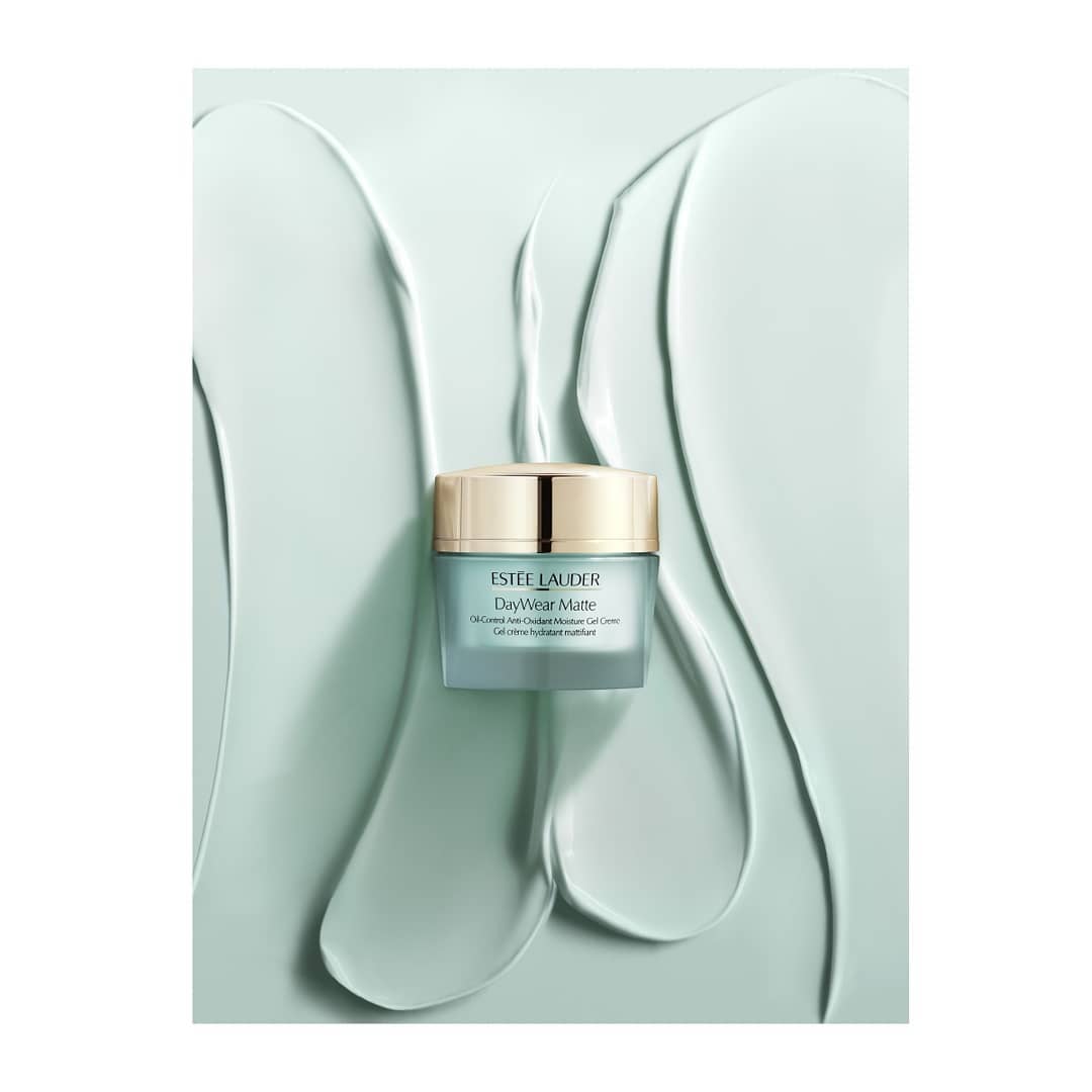 Estee Lauder DayWear Matte moisturizer in a light blue jar with a gold lid on a light turquoise, textured background.