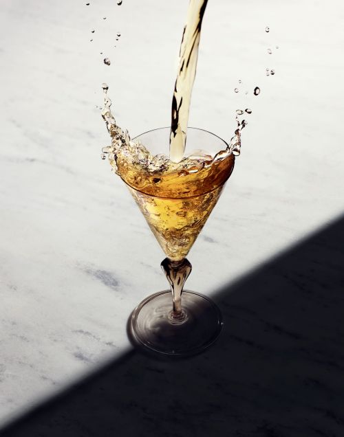 Liquid pouring into a martini glass on a marble surface with a shadow, creating a dynamic splash effect.