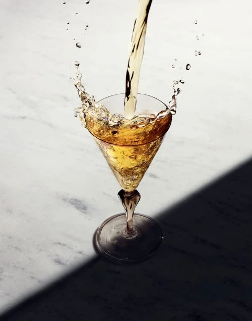 Liquid pouring into a martini glass on a marble surface with a shadow, creating a dynamic splash effect.