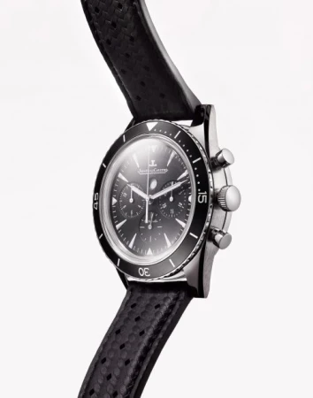Close-up studio shot of a black chronograph wristwatch on a white background, featuring a perforated leather strap and metallic casing.