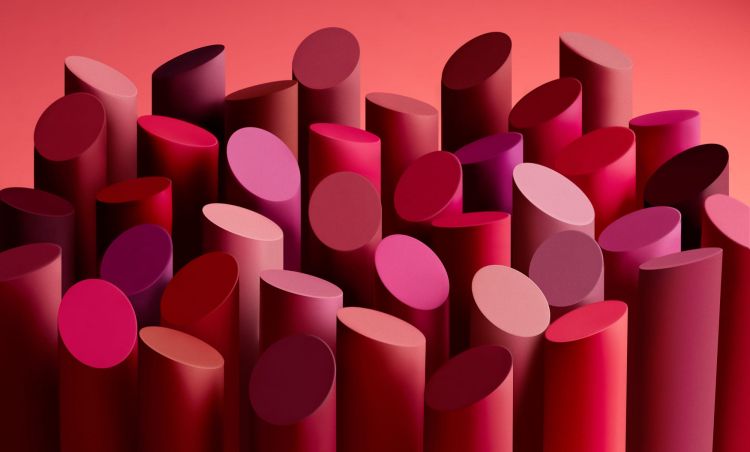 Various shades of red lipstick tubes arranged in an abstract, visually appealing composition against a red background.