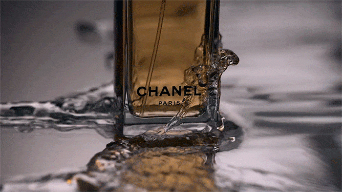 Close-up of Chanel perfume bottle being splashed with water against a grey background in a studio setting for a cosmetic advertisement.