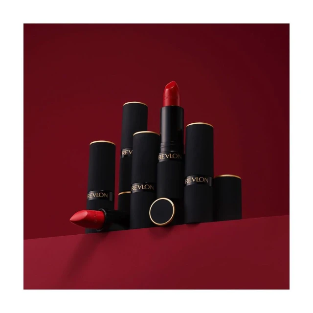 Revlon lipstick products in black and gold tubes with red lipstick, presented on a matching red surface against a red backdrop.
