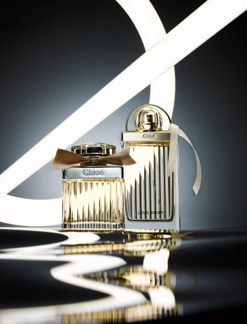 Still life shot of two Chloé perfume bottles with ribbons on a reflective surface with neon lights in the background.