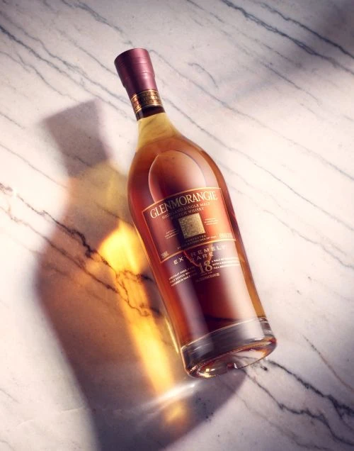 Glenmorangie whisky bottle on a marble surface, lit to highlight its amber liquid and distinctive packaging.