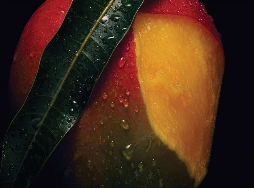 Close-up studio shot of a fresh mango with water droplets on the surface and a green leaf, against a dark background, food photography.