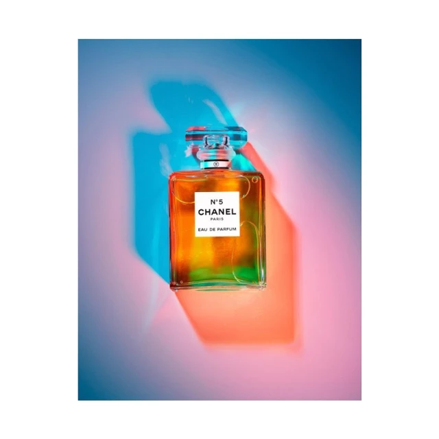 Chanel No. 5 perfume bottle presented against a vibrant backdrop of blue and red light, showcasing its classic design and elegance.
