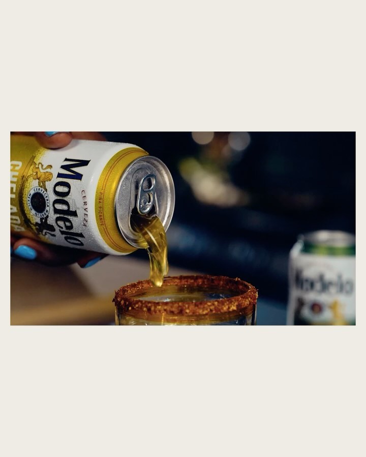 Pouring a Modelo beer can into a salt-rimmed glass, capturing the golden liquid flow against a softly blurred background.
