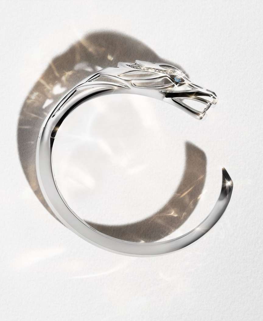 Silver-colored wolf-head cuff bracelet with gemstone eyes, studio product shot on white surface with patterned shadow.