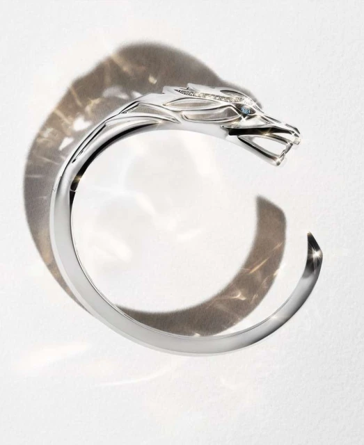 Silver-colored wolf-head cuff bracelet with gemstone eyes, studio product shot on white surface with patterned shadow.