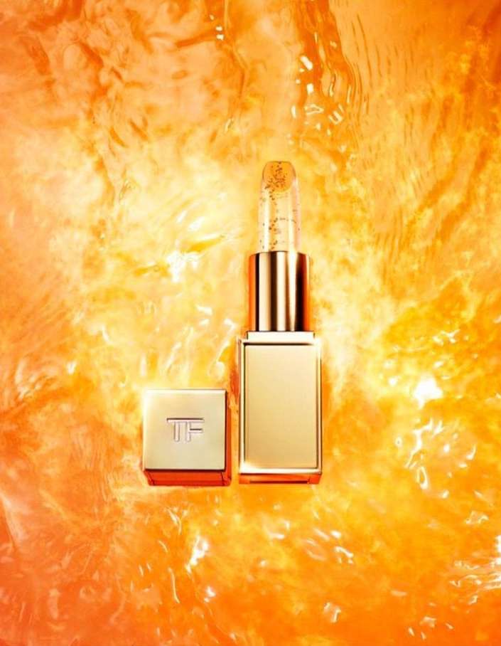 Tom Ford lipstick tube and cap sit on a textured orange background, highlighting the luxurious beauty product and its sleek design.