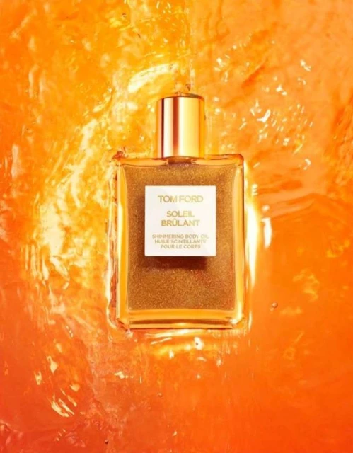 Close-up of Tom Ford Soleil Brûlant shimmering body oil bottle with gold cap on a orange background. Beauty product.