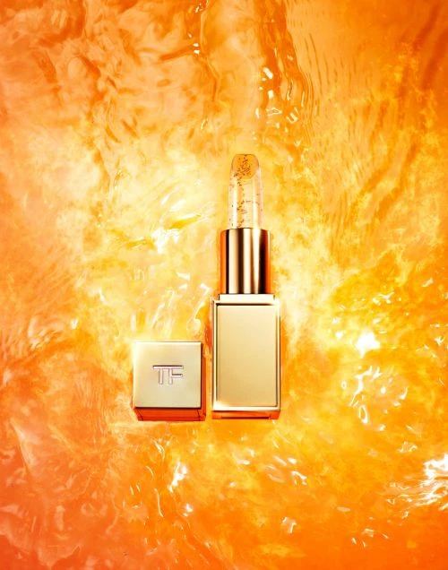 Gold lipstick tube and lid are showcased against a rippled orange water backdrop, highlighting its luxury packaging and reflective surface.