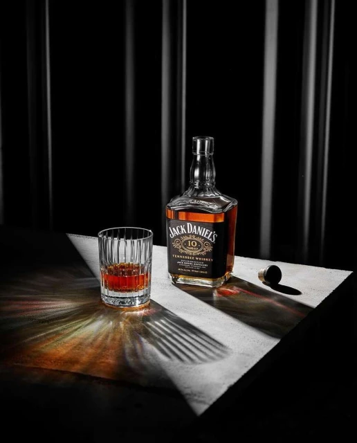 Jack Daniel's 10 year Tennessee whiskey bottle and glass on white table, spotlight, dark backdrop, studio product shot.