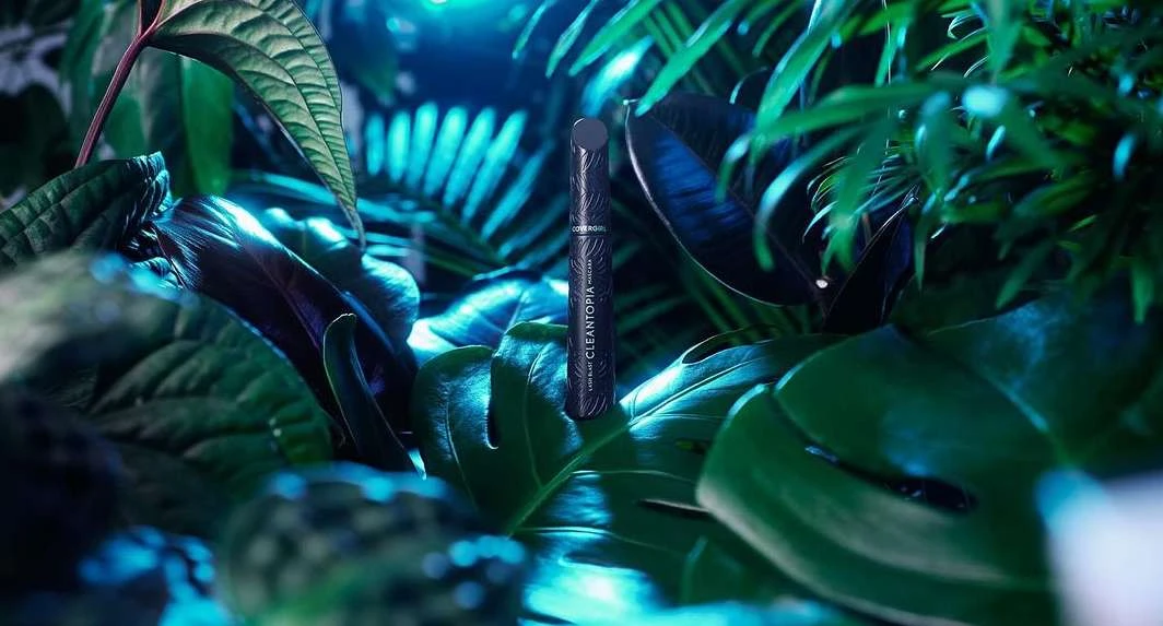 Mascara tube displayed amongst lush tropical foliage under blue lighting, cosmetic product photography, beauty and wellness concept.