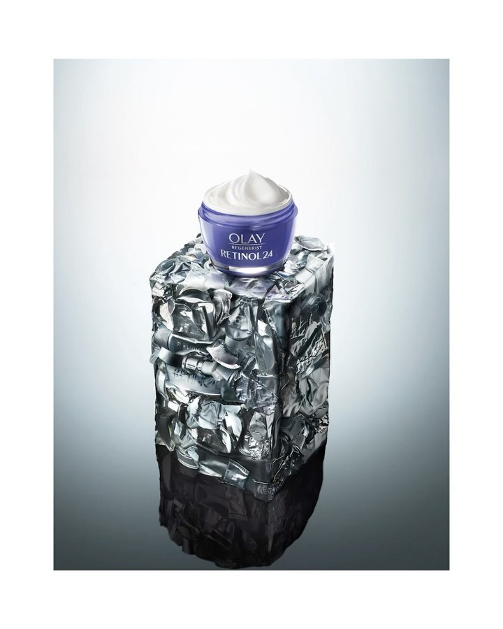 OLAY Retinol 24 cream jar sits atop a block of textured ice in a studio setting with a cool white and gray gradient backdrop.
