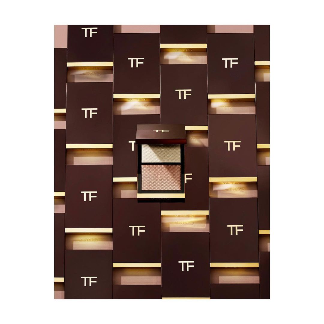 Tom Ford eyeshadow palette with multiple color pans, displayed against a background of TF-branded boxes and gold accents.