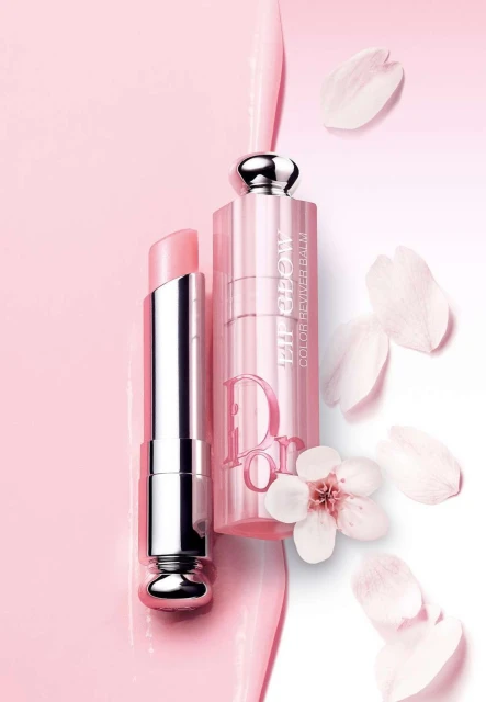 Close-up of Dior Lip Glow and Lip Maximizer in pink packaging with flower petals, studio shot for beauty and fashion advertising.