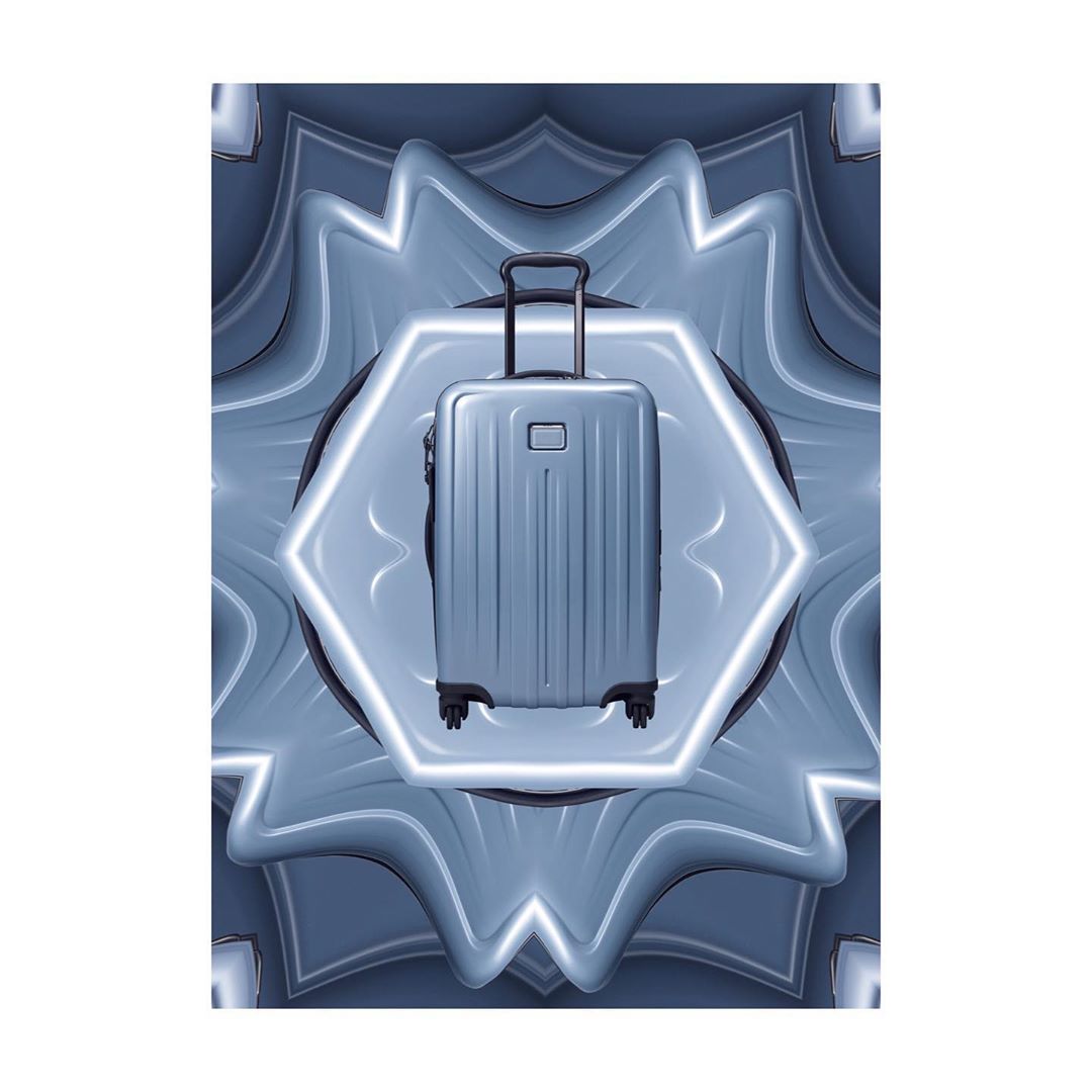 Metallic silver suitcase with extendable handle and wheels, centered on a grey and white abstract background with a starburst effect.