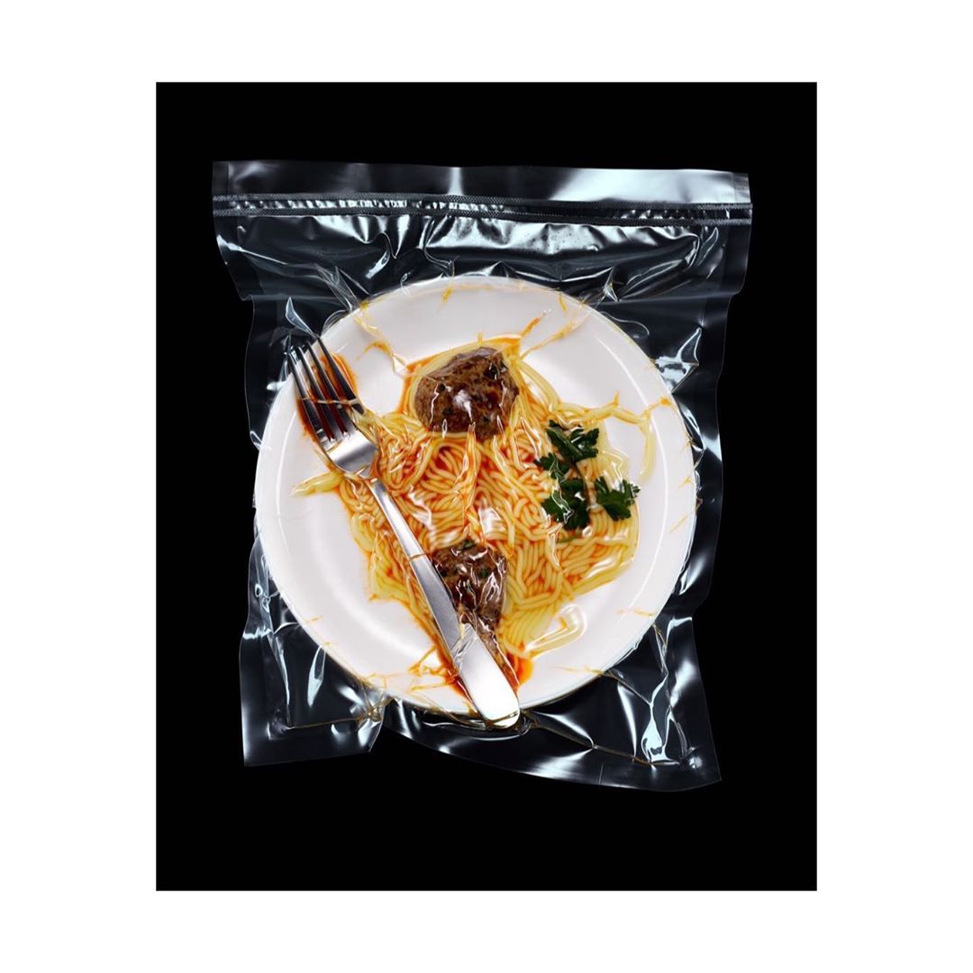 Vacuum-sealed plate of spaghetti and meatballs with a fork, set against a black background. Food is prepared for storage.
