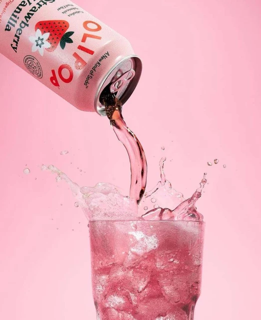 Olipop Strawberry Vanilla drink being poured into a glass of ice against a pink background. Refreshing, fizzy, and visually appealing.