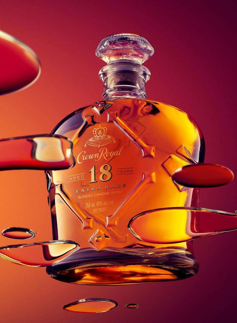 Crown Royal 18 year blended Canadian whiskey bottle close-up on a red gradient background with droplets around the bottle.