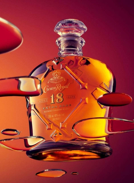 Crown Royal 18 year blended Canadian whiskey bottle close-up on a red gradient background with droplets around the bottle.