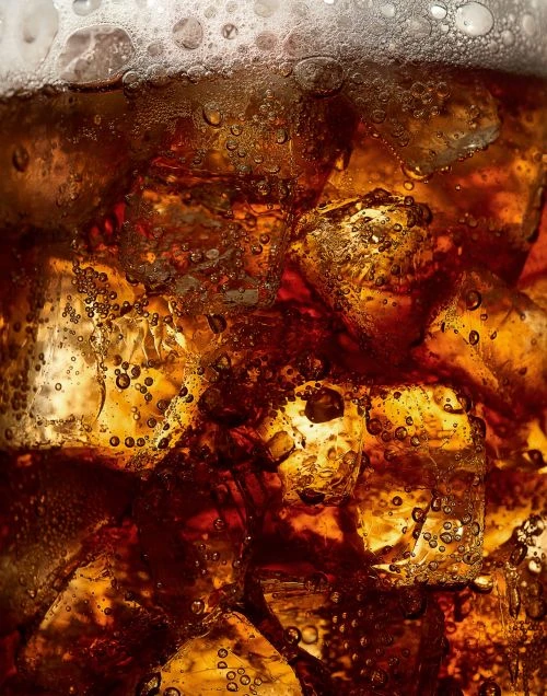 Close-up of a glass filled with cola, ice cubes, and bubbles. Refreshing beverage photography for food and drink industry marketing.