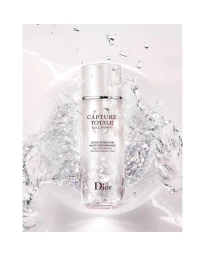 Dior Capture Totale serum bottle surrounded by splashing water droplets against a pale background