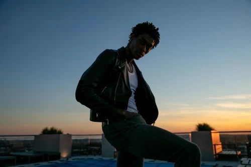 Portrait of a Black man in a leather jacket posing on a rooftop at sunset by photographer Andre L. Perry.