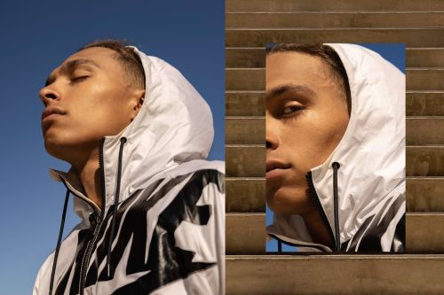 Portrait of a young adult male with eyes closed, wearing a white hooded jacket, set against a blue sky, contrasted with a partial view on steps.