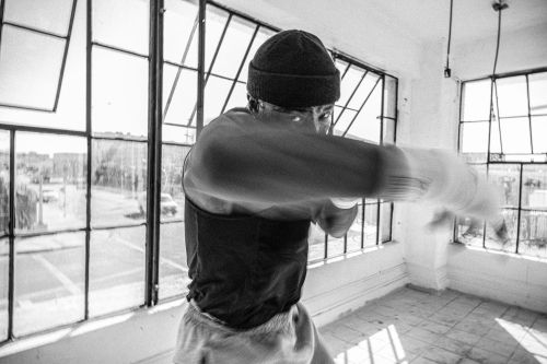 Black and white shot of an adult male punching towards the camera in a workout space with large windows letting in natural light.