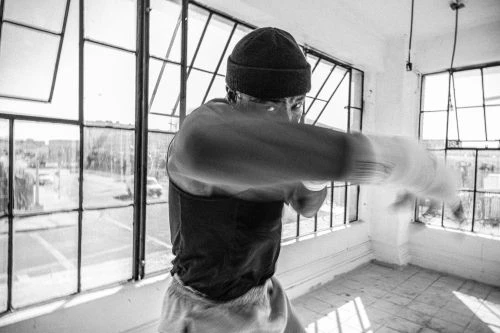 Black and white shot of an adult male punching towards the camera in a workout space with large windows letting in natural light.