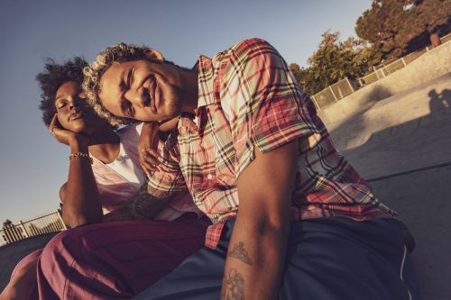 Two people sit together in outdoor skate park. A man and a woman with arms around each other, enjoying warm sunlight and casual style.