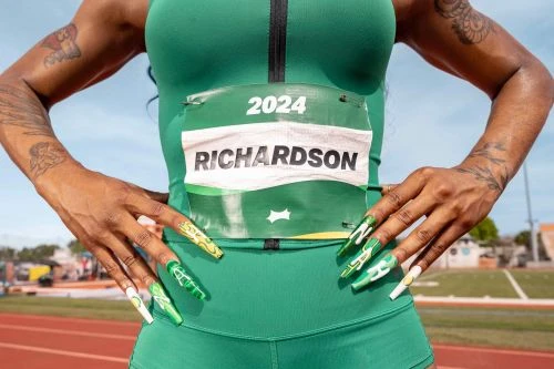 Close-up of a female athlete in a green running suit, wearing a bib labeled 'RICHARDSON 2024,' posing on a track with elaborate green and white nails.