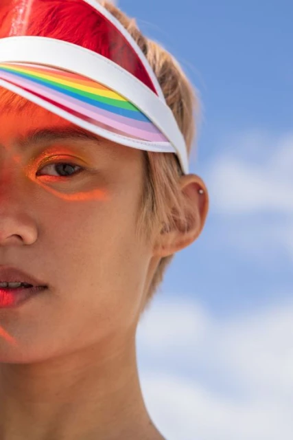 Close-up of a person with short hair wearing a colorful visor against a blue sky with clouds, showcasing fashion and beauty.