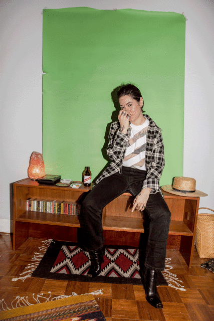 Young adult woman posing on a mid-century modern shelving unit with a green backdrop, illuminated by soft, diffused light in a room.