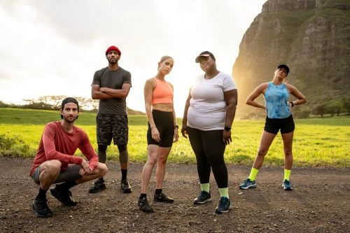 Group of five diverse adults in athletic wear stand on dirt path in a field near mountain, preparing for outdoor exercise.