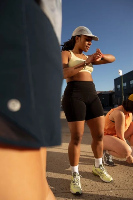 African-American woman in workout clothes checks watch with two other women on the sidewalk on a sunny day in an urban setting.
