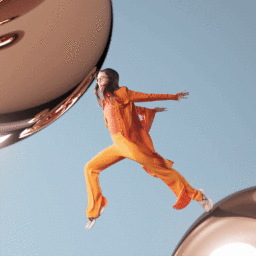 Woman wearing an orange suit leaping between large reflective bronze spheres against a blue background