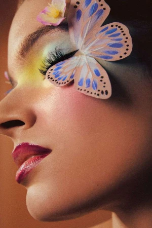 Close-up profile of a woman with pastel eye makeup, fake eyelashes, and a paper butterfly and flower attached to her face by Brittany Bravo.