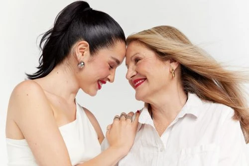 A profile shot of two women of different generations in light-colored clothing, with their foreheads touching in a light, bright indoor setting.