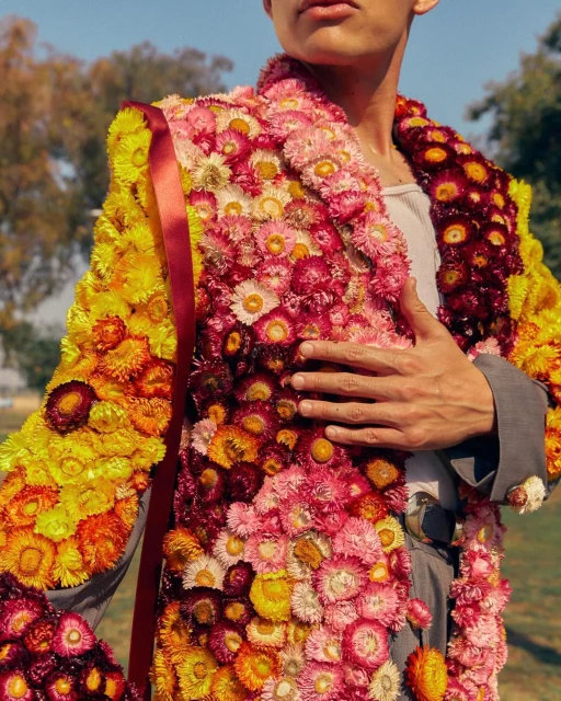 Person wearing a flower-covered blazer outdoors with trees and sky in the background, showcasing a unique and creative fashion statement.