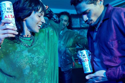 Young people holding Tecate Alta cans at a party under blue and green neon lighting, photographed by Brittany Bravo