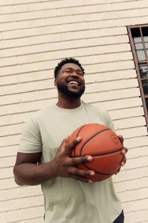 Portrait of a smiling Black man holding a basketball against a light brick wall in Los Angeles by Brittany Bravo.