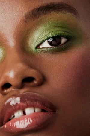 Extreme close up beauty portrait of a Black woman with shimmery green eyeshadow and glossy nude lips photographed by Brittany Bravo.
