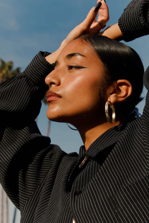 Portrait of a dark-haired young woman in a striped shirt against a sunny sky. She is adorned with gold hoop earrings.