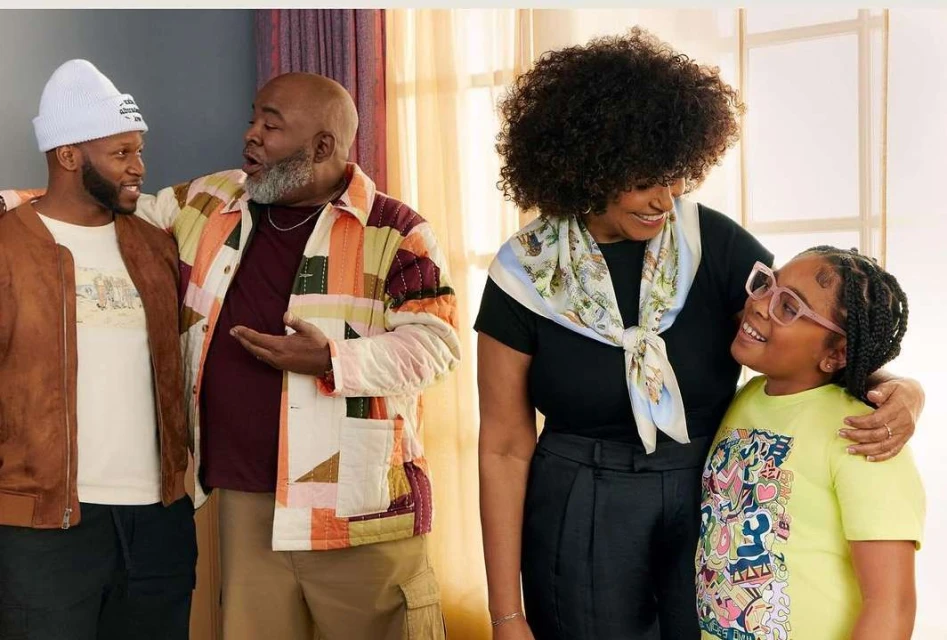 Indoor portrait of a multi-generational family of five, featuring two adult men, an adult woman, and a girl and a young child, smiling.