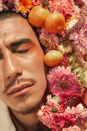 Close-up portrait of a man with closed eyes framed by lush pink flowers and oranges by Brittany Bravo