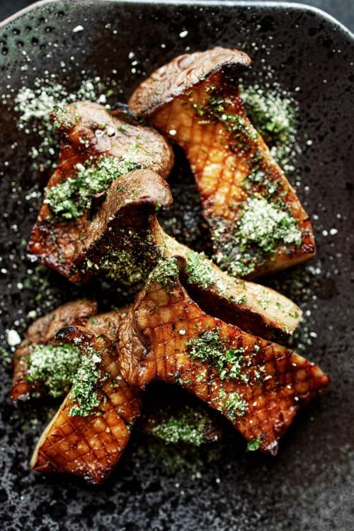 Overhead shot of cooked king oyster mushrooms drizzled with green sauce, presented on a dark plate, creating an appetizing culinary still life.
